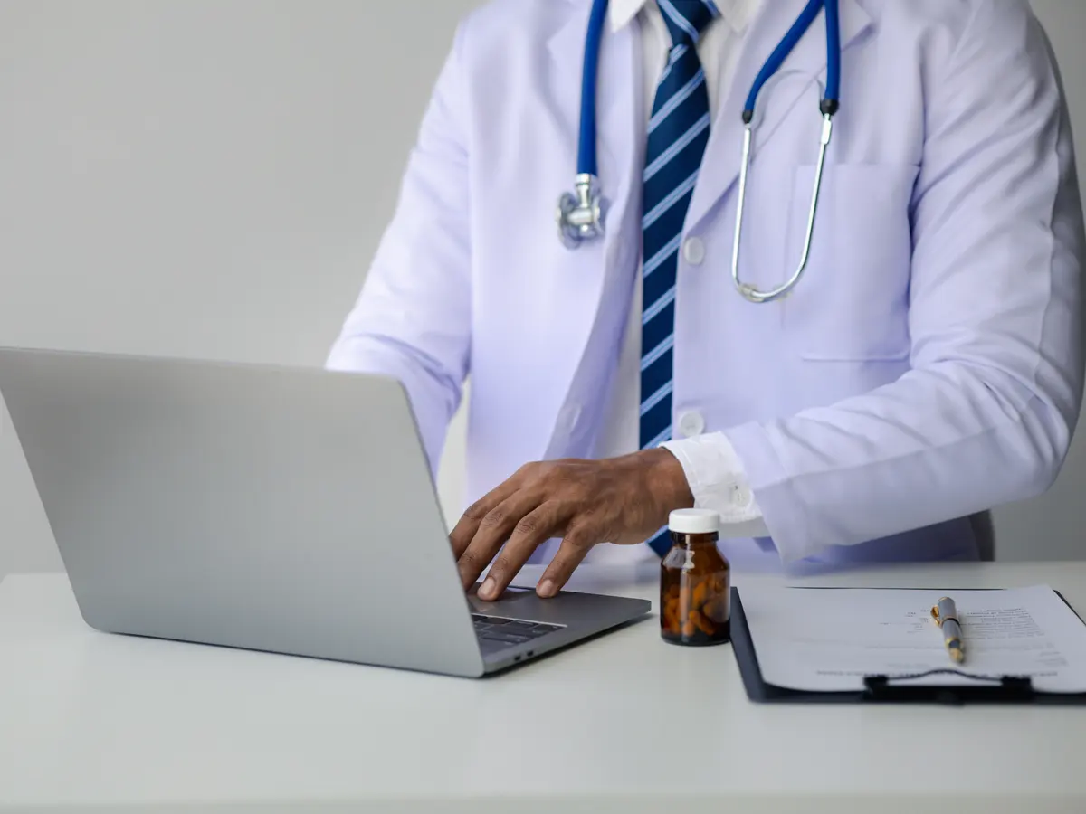 Person filling out paperwork next to a laptop
